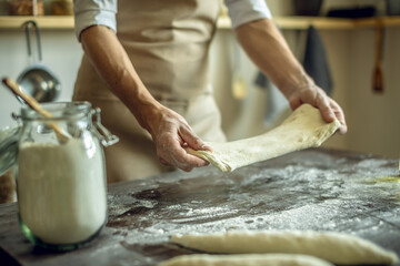 A baker in an apron kneads the dough with his hands and sprinkles it with flour to bake delicious homemade bread.