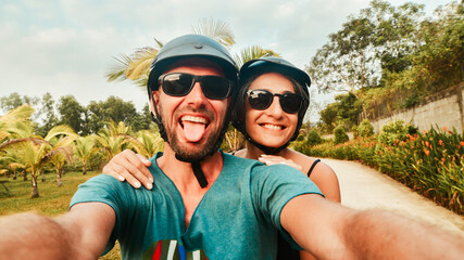 Portrait crazy smiley young happy caucasian couple take smartphone selfie while having fun driving scooter on tropical road trip in southeast asia. Couple in love having fun travel in asia
