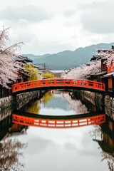 Japanese cherry blossom bridge over a calm waterway, reflected  Traditional wooden buildings along the canal banks