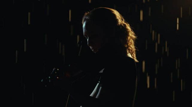Romantic music in night rain, female violinist playing melody in darkness. Portrait of talented young woman performing classical music, contemporary performance, mysterious female silhouette in dark