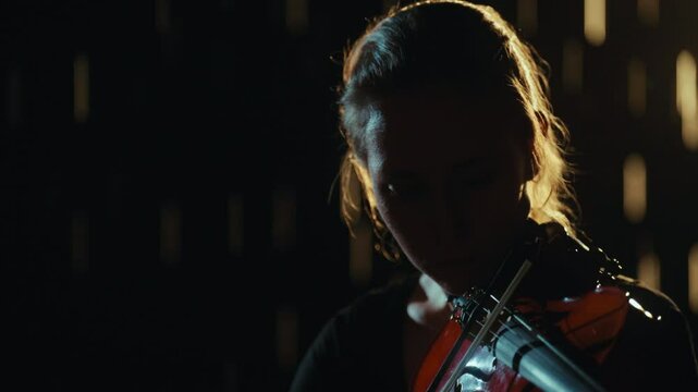 Mysterious silhouette of young woman playing violin in dark, music in night rain . Talented female violinist performing classical music, contemporary performance on theatre stage or street in night