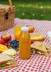 Picnic basket with juice bottle, sandwiches, and fruit on checkered tablecloth