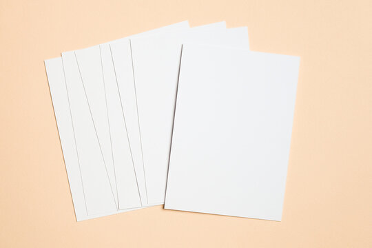 Fanned stack of blank white cards displayed on a beige background, perfect for showcasing invitation mockups, minimalist stationery, or print designs