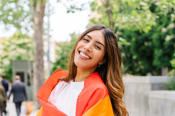 Happy young woman draped in rainbow flag, radiating pride and celebrating lgbtq+ equality in sunlit...