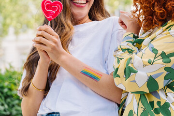 Lesbian couple embracing, showcasing rainbow tattoo and heart lollipops, expressing intimate connection and lgbtq pride with tender closeness and shared happiness