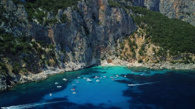 Aerial view of a beautiful rugged coastline with a turquoise cove and floating boats.