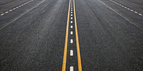 Asphalt road surface with clear dashed white and solid yellow lines, showing symmetrical top down view of textured pavement, evoking sense of direction and structure