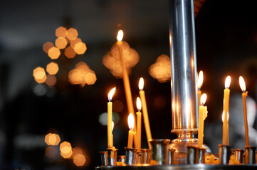 Burning church candles in a contemplative and serene setting surrounded by soft, warm bokeh lighting. A peaceful and spiritual representation of light in the darkness, inspiring calmness.