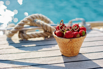 Fototapeta premium Basket of Fresh Strawberries with Decorative Love Sign by the Waterside..