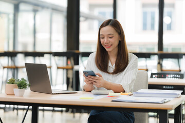 Fototapeta premium Smiling Asian Woman Using Smartphone at Desk