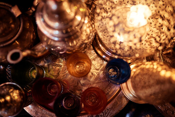 Top view of colorful glass cups and ornate metal teapots on a decorative tray.