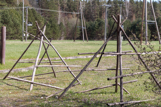 
Two structures made of tree branches, possibly some kind of temporary structure or support, located in a grassy field with trees and electricity poles in the background.