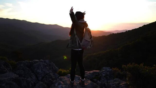 Una mujer triunfal en la cornisa de una monta&ntilde;a rocosa, con los brazos extendidos ante un impresionante atardecer de fondo. 