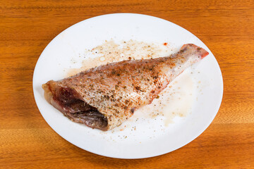 Raw redfish carcass marinated in spices on dish on table