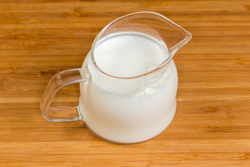 Milk in the small glass jug on a wooden surface