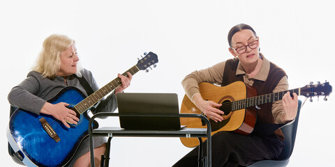 Obraz premium Elderly women playing acoustic guitars while studying music together with laptop during online lesson against white studio background. Concept of creative learning, education, friendship, aging.