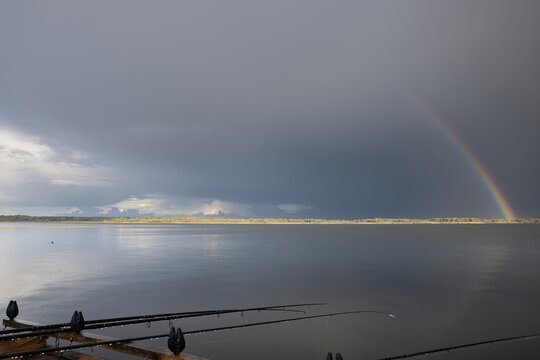 Fishing rods on pier over lake with double rainbow after rain, peaceful natural landscape