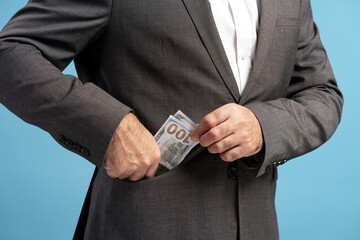 Businessman putting dollar banknotes into pocket of his suit