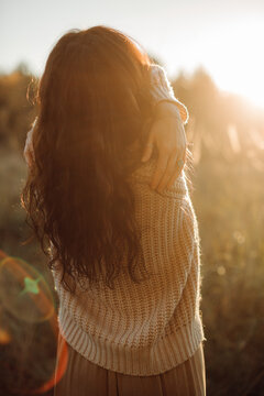 Woman hugging herself enjoying golden hour sunlight in nature