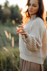 Woman wearing knitted sweater touching dry grass in nature at sunset
