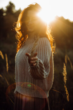Young woman wearing knitted sweater enjoying golden hour sunlight in a field