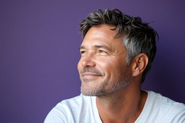 Fototapeta premium A glowing and peaceful man expressing warmth. Concept layout of style for aging men. Purple solid background. Modish men's side part haircut - midlife white man with hair.