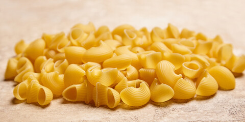 Wide-angle shot of uncooked pipe rigate pasta with ribbed, golden yellow curves resting on a light stone background, ideal for culinary or packaging themes