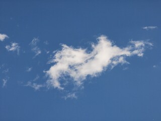 A single irregularly shaped fluffy white cloud drifts in a bright blue sky, creating a peaceful and airy natural sky background