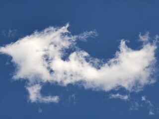 Distinctively shaped white cloud with uneven, jagged edges floats against a vivid blue sky, creating an airy and imaginative sky background