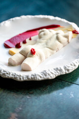 A creative dessert featuring a sculpted figure made from sweet ingredients, paired with vibrant sauces on a decorative plate, highlighting artistic culinary presentation.