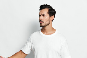 Stylish man with a serious expression wearing a plain white t-shirt, posing confidently with his hand raised, isolated on a minimalist solid background. Fashion portrait concept.
