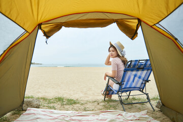 Young woman sitting on a beach chair inside a tent, relaxing and enjoying the ocean view