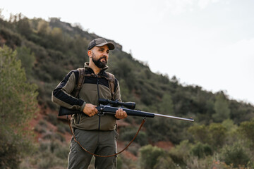 Hunter holding rifle while standing on mountainside