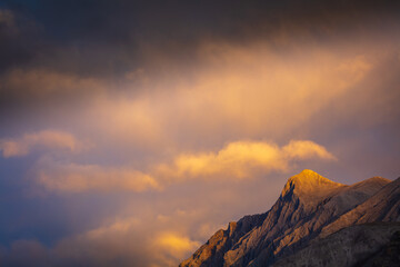 Sunset over the barren mountains of Muncho Lake Provincial Park, British Columbia Canada; last rays of the setting sun illuminate the clouds above a mountain peak