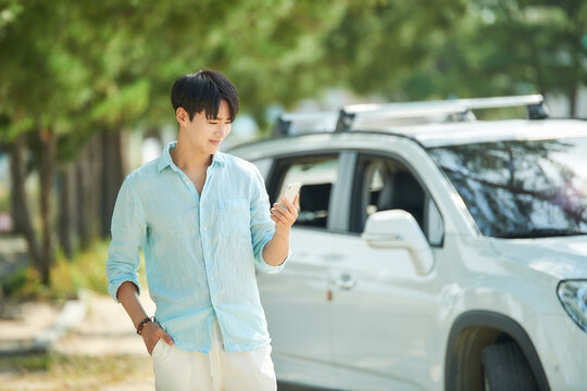 Young Man Using Smartphone Outdoors Near Car
