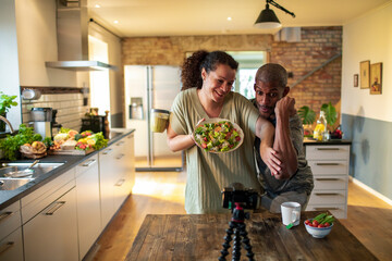 Middle aged couple recording and streaming a healthy salad recipe tutorial in the kitchen