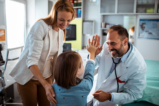 Smiling doctor using stethoscope to check young girl at medical clinic with mother nearby