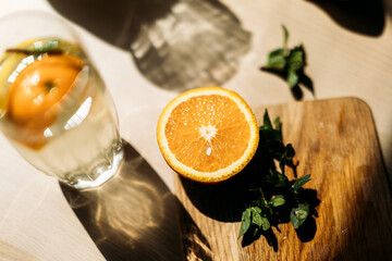 A halved orange resting on a rustic wooden board, accompanied by fresh mint leaves. Sunlight...