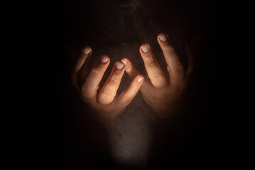Hands in prayer, Hands of a person in prayer with a rosary in a dark and smoky place, low key portrait, selective focus.