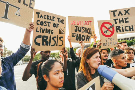 Crowd of multiracial people protest against inflation and financial crisis - Protesters marching for rise cost of living - Focus on center banners