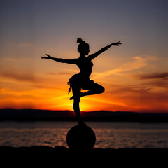 Silhouette of female acrobat balancing on ball against vibrant sunset background