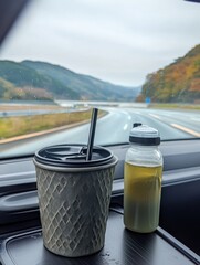Iron water cup with handle and lid on car dashboard, green tea inside, gray metal texture, highway scenery through window, black straw and plastic bottle
