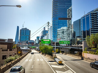 Obraz premium Elevated highway in Sydney, Australia leading toward the Harbour Bridge and city center, surrounded by modern skyscrapers and road signs—themes of urban infrastructure, transport and urban planning