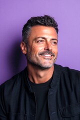Fototapeta premium A handsome man with a captivating smile. Purple solid background. Creative of style for aging men. Fashionable men's shoulder-length taper haircut - midlife white man with black hair.