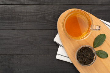 Cup of tea with dry and fresh leaves on wooden background, top view