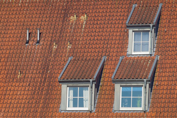 Three dormer windows and two chimneys emerging from red tile roof