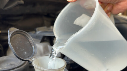 Pouring antifreeze Filling a windshield washer tank with an antifreeze. Pouring liquid into car washer tank to clean the windshield. hands pour water from bottle