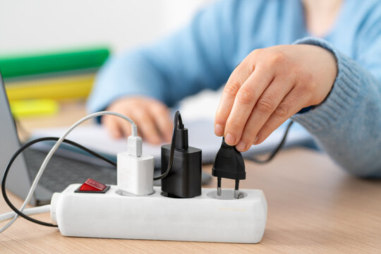 Close up of female student hand plugging plug on a power strip socket using laptop on a desk at home
