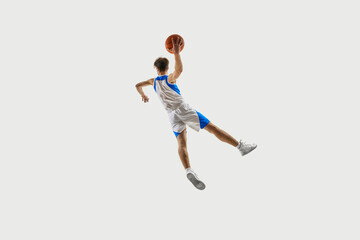 Peak tension moment. Basketball player flying backward in twisting leap, hand stretched up gripping ball against white background. Concept of sport championship, tournament, game, training. Ad
