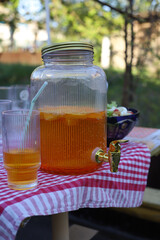picnic in the village in the yard of the house. glass jar with a tap and an orange refreshing drink on the table and a glass with a straw next to it